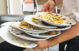 Hospitality worker carrying stacked plates of uneaten food waste from a restaurant table