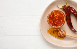 Bowl of chilli infused hot honey with dried chillies and a wooden honey dipper