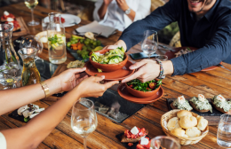 Group of people sharing small plates of food at a restaurant table, surrounded by wine glasses and appetisers.