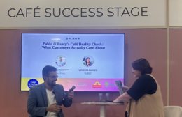 Photo of two people seated on stage at the Café Success Stage during Food & Hospitality Week, with a presentation slide visible reading 