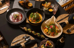 Table spread of modern Vietnamese dishes at QT Kitchen, including small plates, a curry bowl and fresh herb garnishes served on a dark table setting.