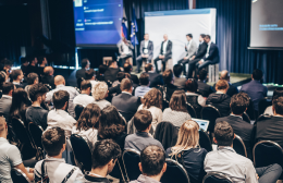 Audience seated at an industry conference panel session, with speakers on stage discussing hospitality industry topics.
