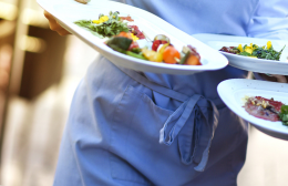 Server carrying plates of fresh salad and garnished dishes at a busy restaurant