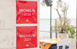 Red Michelin Guide 2026 and 2025 plaques on a stone wall beside a sunlit outdoor dining terrace overlooking the sea