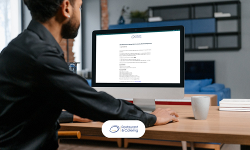 A hospitality operator sitting at a desk reviewing the R&CA Industry Benchmarking Survey on a desktop computer, representing industry participation in the 2025 survey.